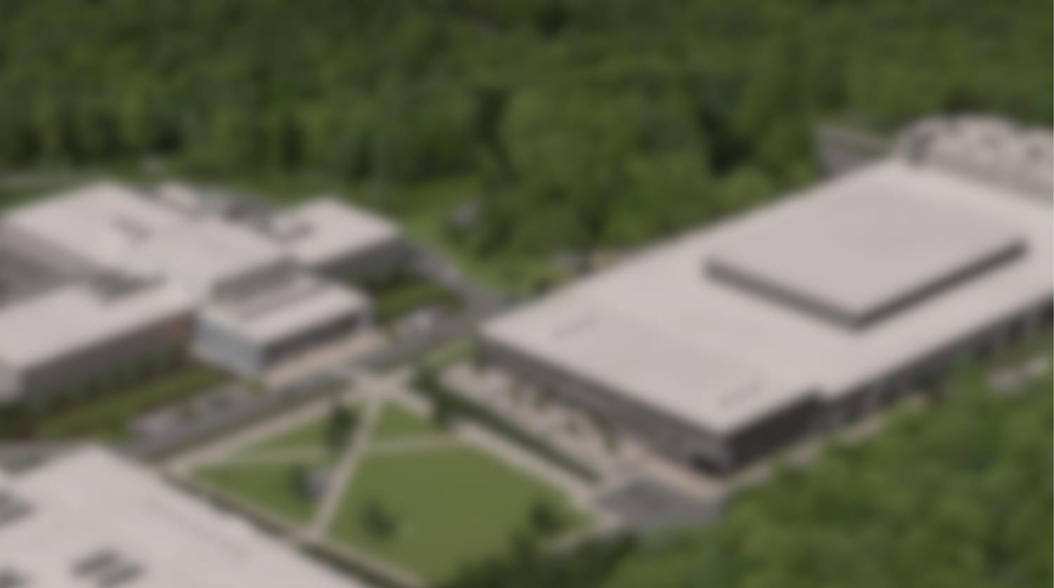 Aerial rendering of the build-to-suit magnet manufacturing campus — a long low-rise plant beside an existing complex, around a landscaped green in wooded countryside
